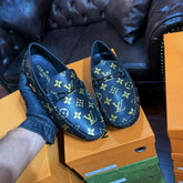 Blue loafers with a pattern on an orange shoe box, with a black leather sofa and boxes in the background.